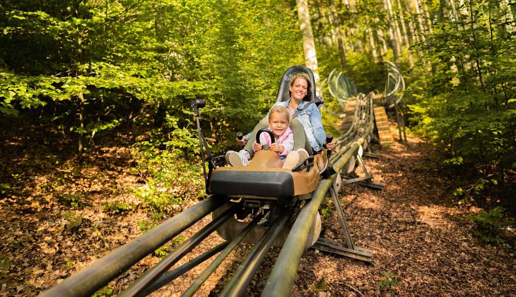 Die Mutter passt auf Ihre lächelnde Tochter in der Sommerrodelbahn auf.